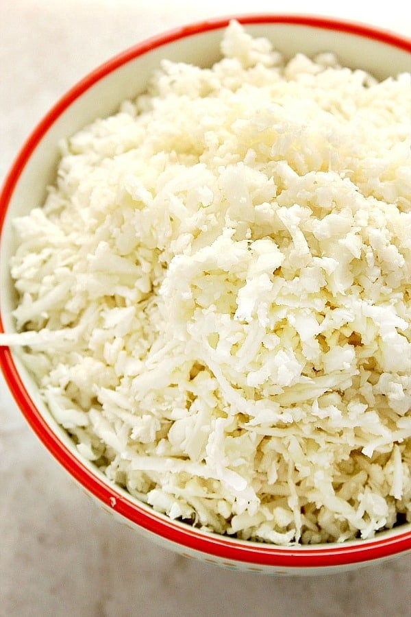 Close up shot of cauliflower rice in bowl with red rim.