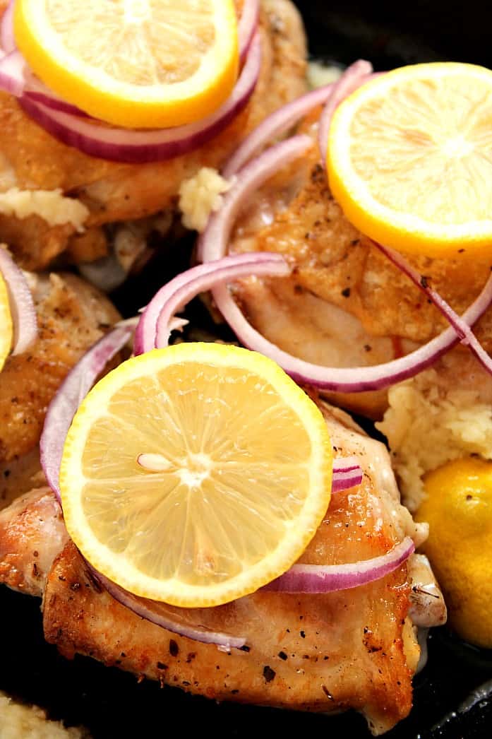 Chicken thighs with lemon slices arranged in pan.