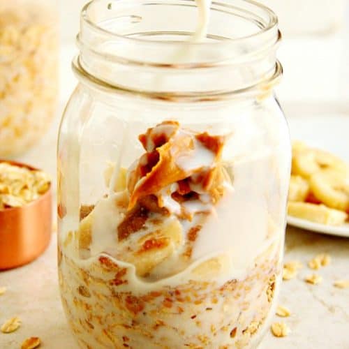 Oats and peanut butter in glass jar, milk being poured in.