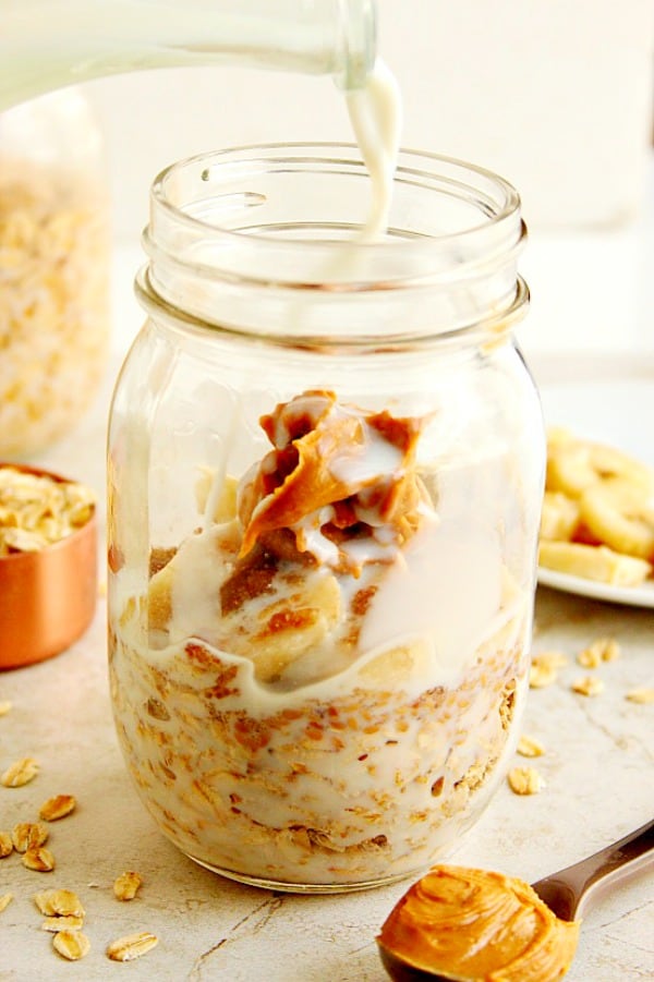 Side shot of oats with peanut butter in jar, with milk being poured in.