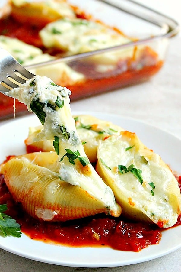 Stuffed Pasta Shells recipe Pasta Shells on a white plate with tomato sauce underneath.