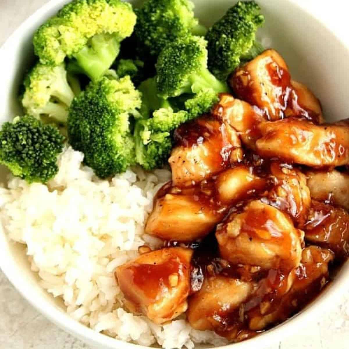 Square image of chicken in teriyaki sauce, rice and broccoli in a white bowl.