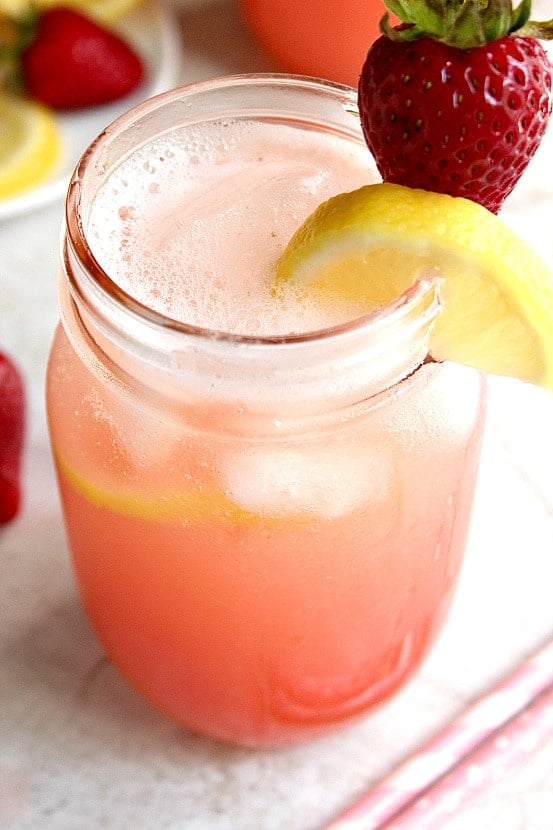 Strawberry lemonade with lemon wedge and fresh strawberry on the rim.