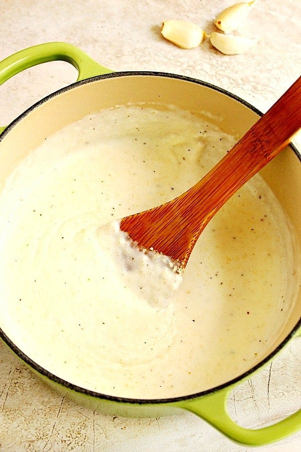 Overhead shot of white sauce in saucepan with wooden spoon inside.