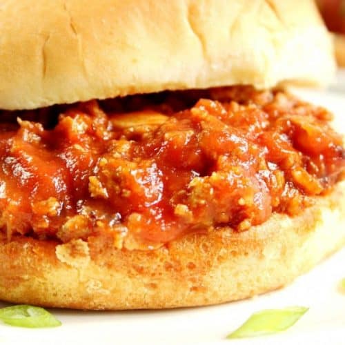 Side shot of Sloppy Joes in bun on white plate.