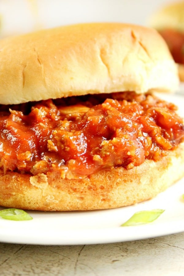 Side shot of Sloppy Joes in bun on white plate.