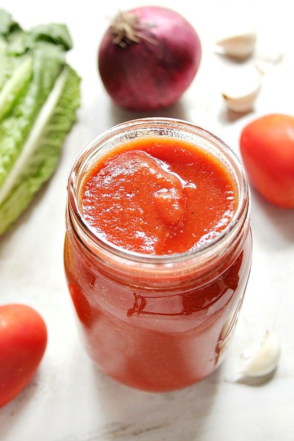 Red sauce in glass jar, with vegetables around it.
