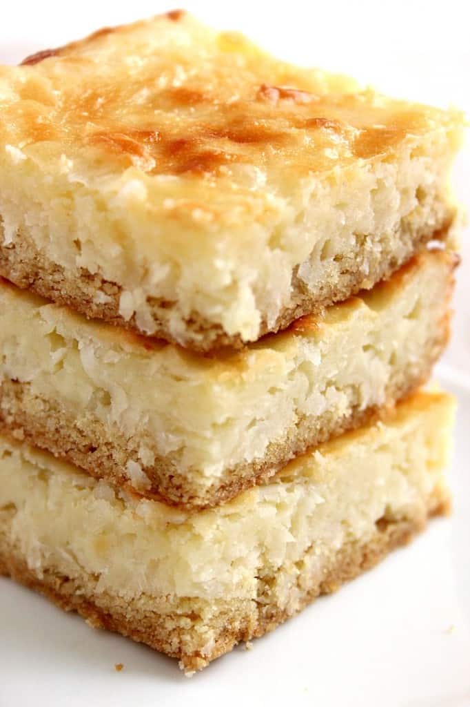 Side shot of three coconut cheesecake squares stacked up on each other.
