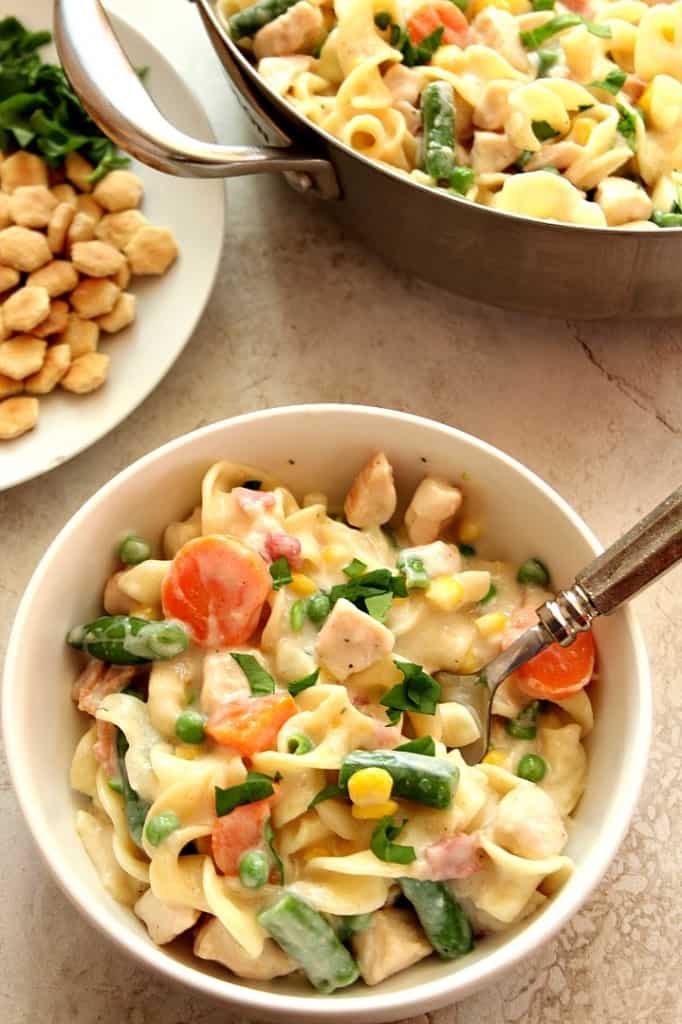 Overhead shot of chicken pot pie pasta in white bowl with skillet in the background.