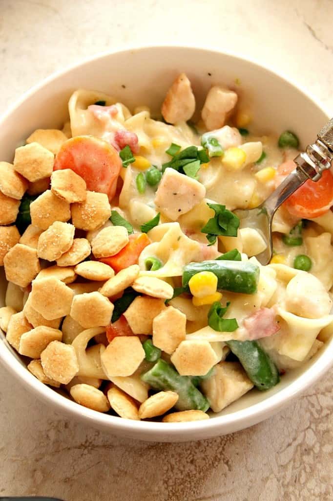 Overhead shot of chicken pot pie pasta with oyster crackers in white bowl.