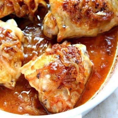 Square photo of roasted chicken thighs with onions and sauce in a Dutch oven.