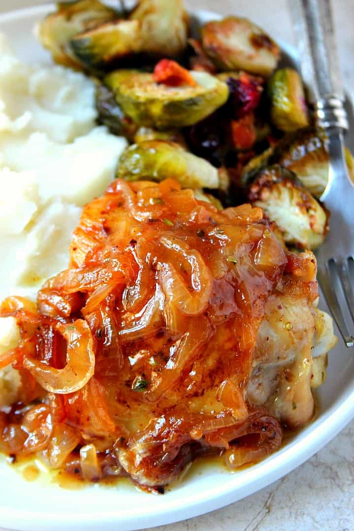 Close up shot of French onion roasted chicken on white plate, with Brussels sprouts in the back.