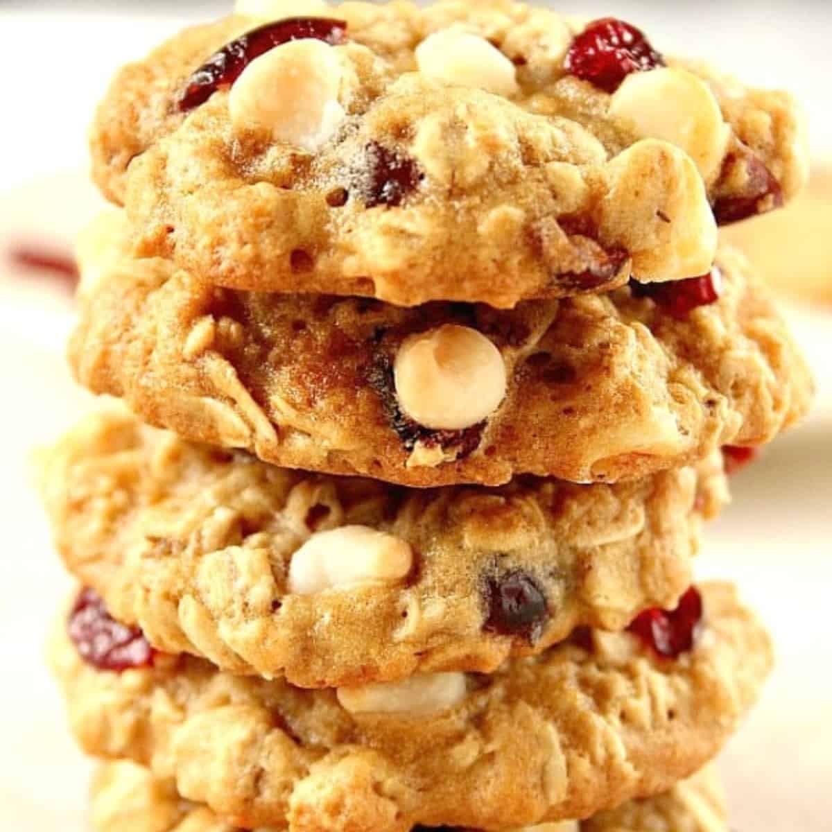Square image of oatmeal cookies with white chocolate chips and dried cranberries stacked up on a plate.
