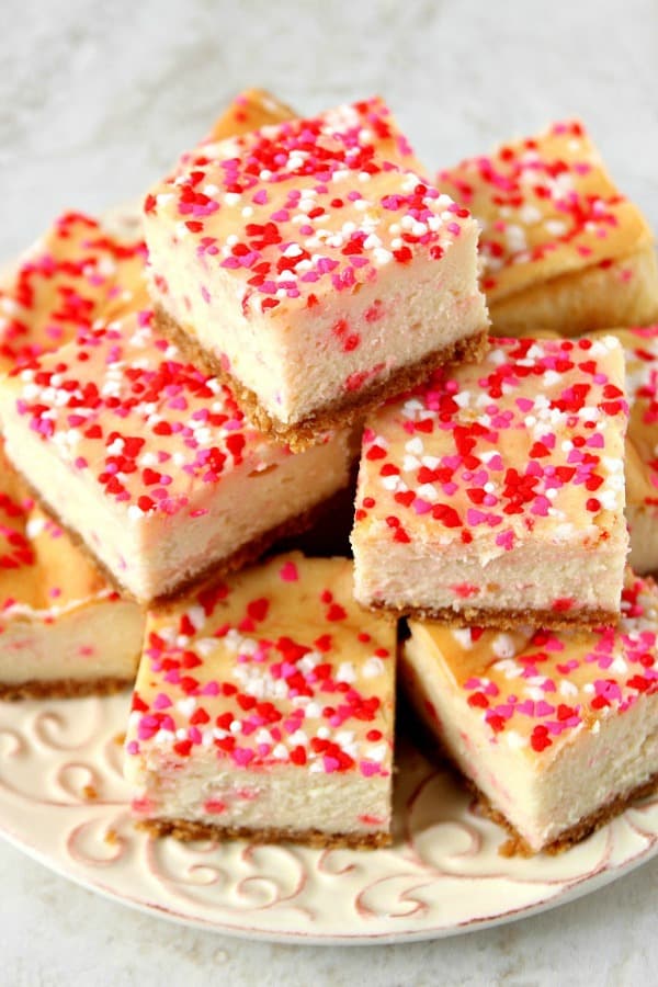 Funfetti Cheesecake Bars Recipe - sweet, creamy and thick cheesecake bars with sprinkles! So fun and festive and super easy to make! Funfetti Cheesecake Bars stacked up on a white plate.