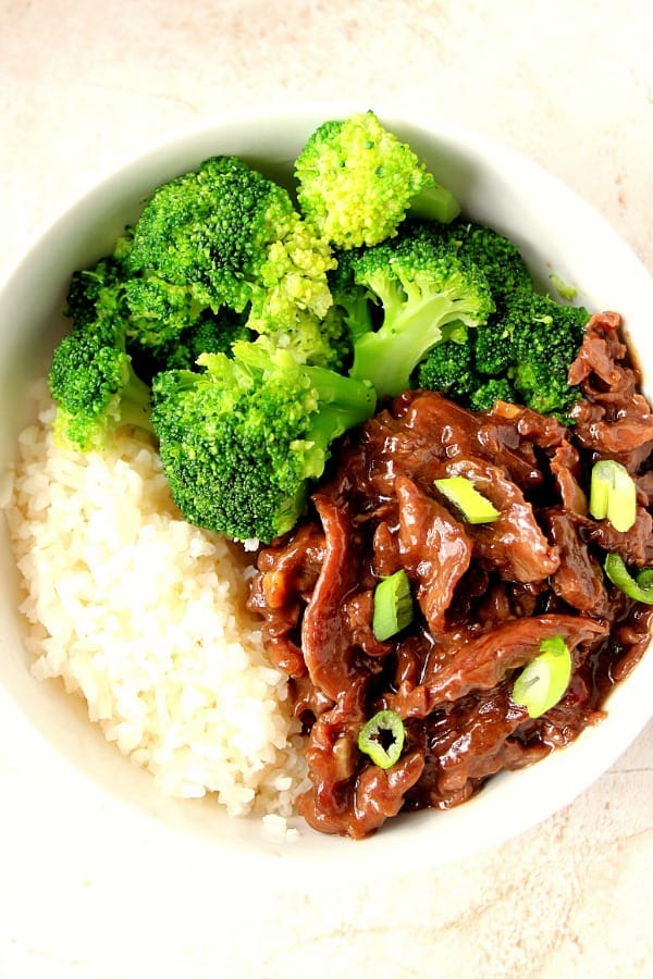 Mongolian Beef over rice with broccoli in white bowl.