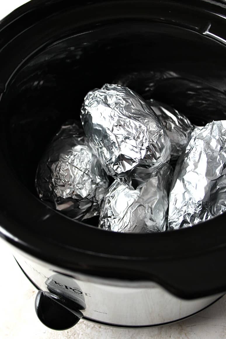 Side shot of potatoes wrapped in foil, set in slow cooker.