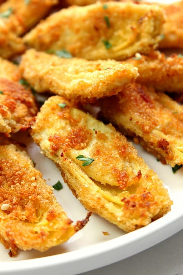 Baked Artichoke Hearts Recipe - delicious appetizer idea that couldn't be easier to make! Artichoke hearts dipped in garlicky butter and coated with Parmesan breadcrumbs. Baked to crispy perfection! Baked Artichoke Hearts on white plate.