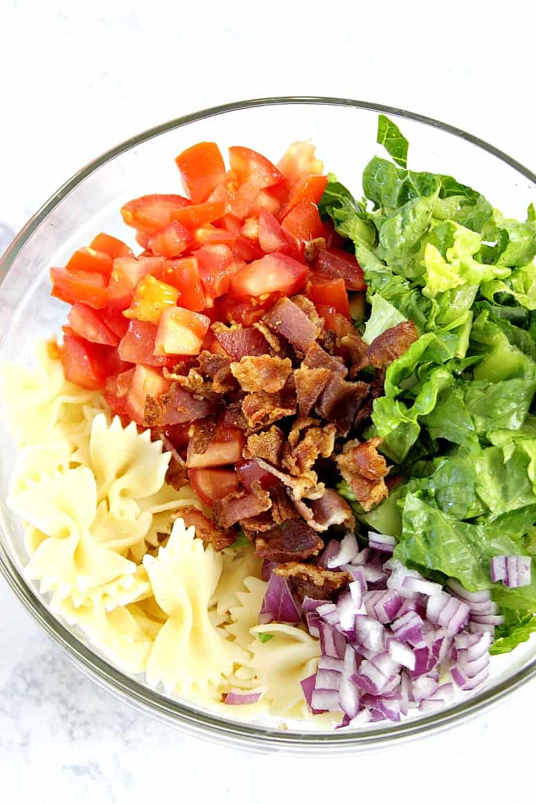 Overhead shot of ingredients for pasta salad in glass bowl.