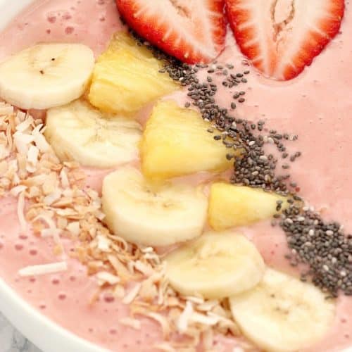 Strawberry smoothie in a bowl with pineapple and banana slices on top.