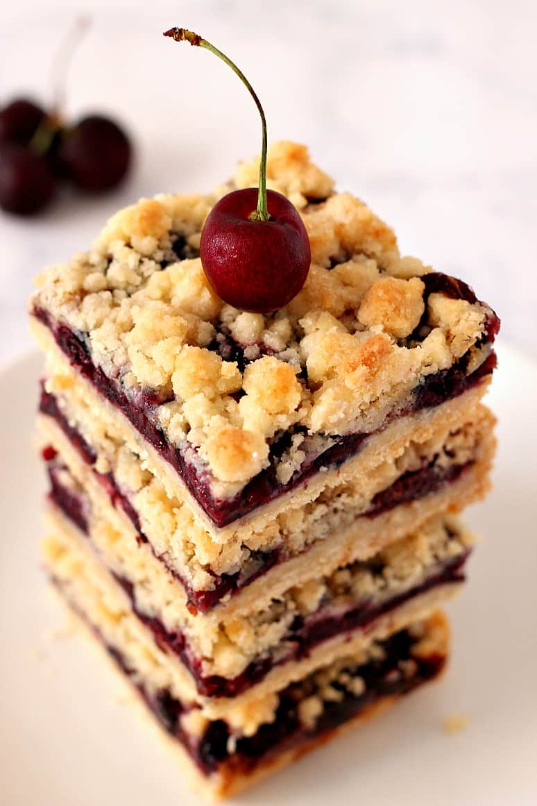 Close up of cherry crumb bars stack with a fresh cherry on top.