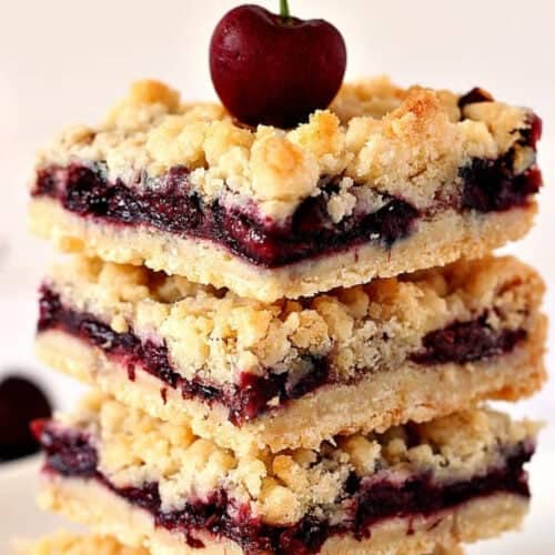 Square image of cherry crumb bars stacked with a fresh cherrie on top.