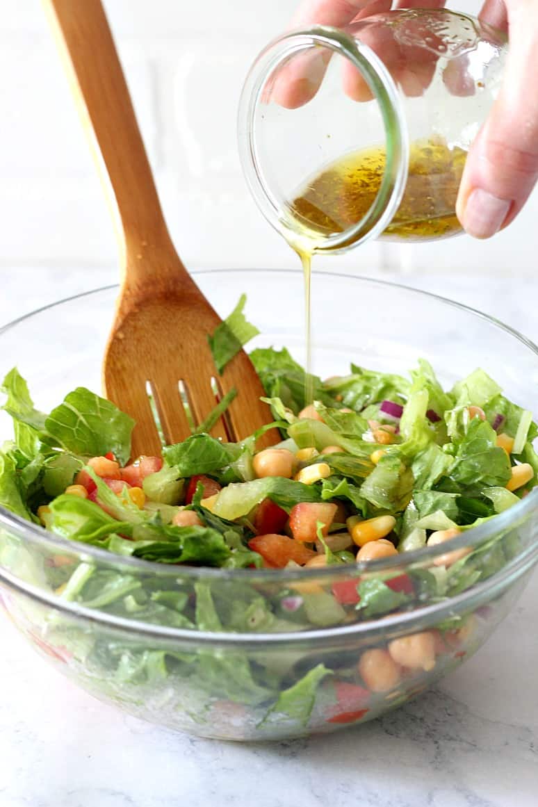 Salad in a glass bowl with dressing pouring in.