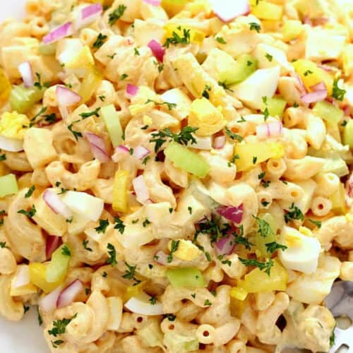 Square image of macaroni salad with hard-boiled eggs in a white bowl.