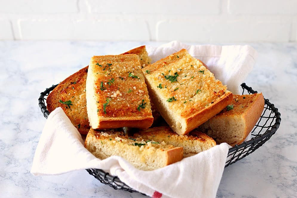 Horizontal shot of garlic bread pieces in black wire basket.