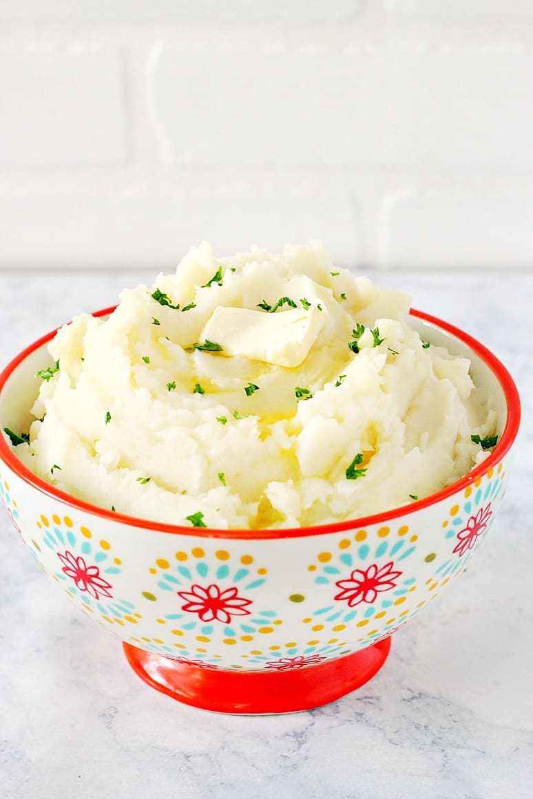 Mashed potatoes with a piece of butter in a bowl with red rim.