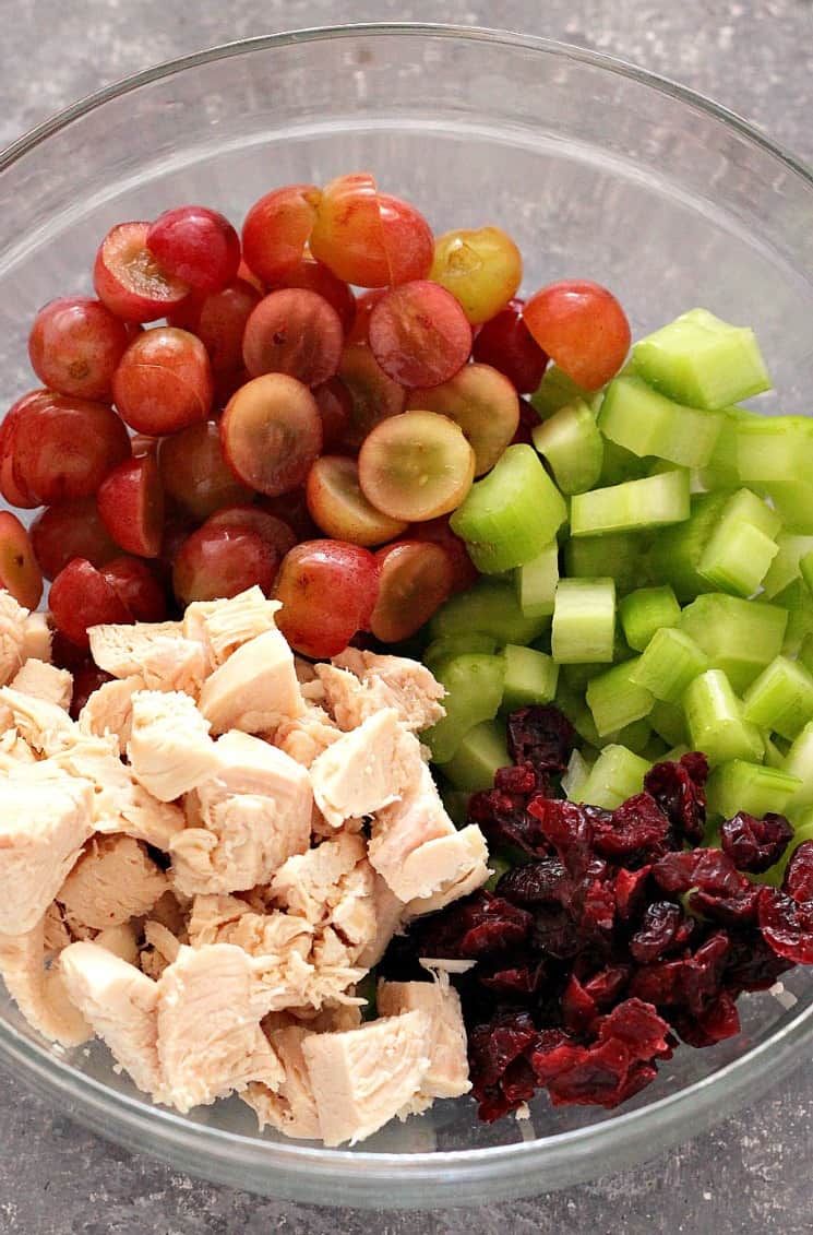 Overhead shot of cubed chicken, grapes, celery and craisins in glass bowl.