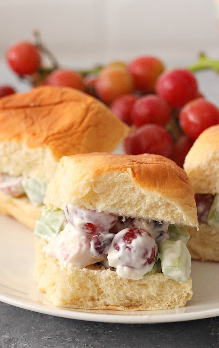 Side shot of Hawaiian rolls with chicken salad with grapes on white plate.