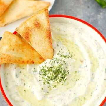 Overhead shot of tzatziki sauce in bowl, with pita chips dipped.