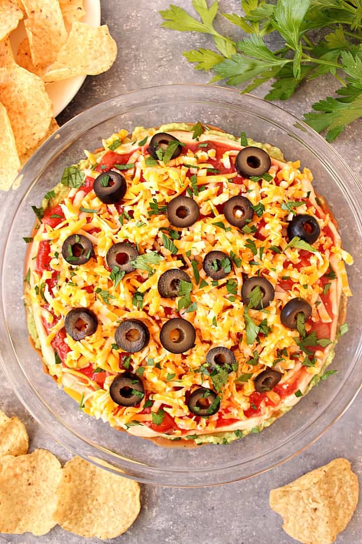 Easy Mexican Layer Dip in glass bowl with chips around it.