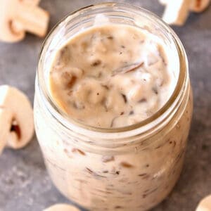 Square image of homemade cream of mushroom soup in a glass jar on a gray board.
