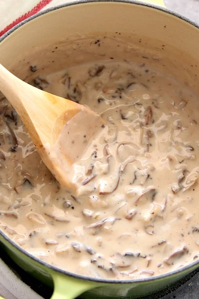 Cream of mushroom soup in a green Dutch oven on a gray board.