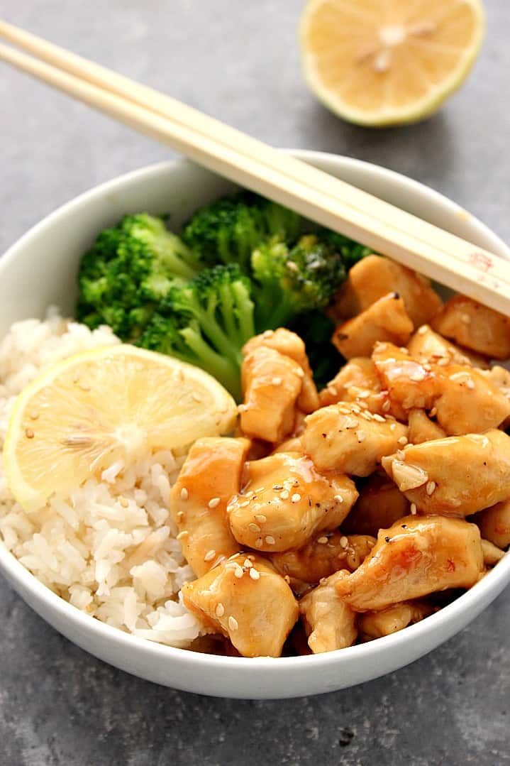 Side shot of honey lemon chicken in bowl, with rice and broccoli. Chopsticks set on the edge of the bowl. 