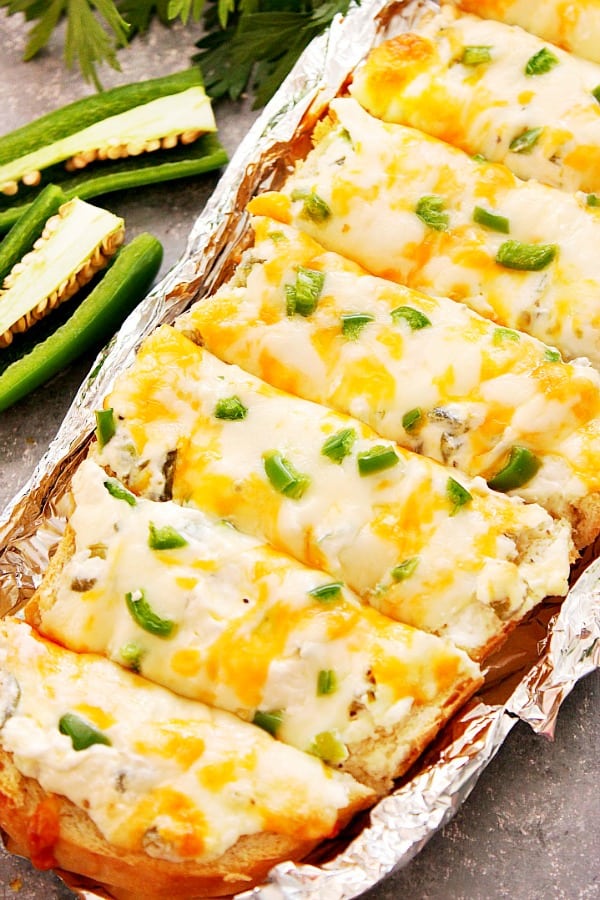 Cheesy Jalapeno Popper Bread Recipe - crispy baked bread topped with jalapeno popper mixture, cheese and fresh chopped peppers. Jalapeno Popper Cheesy Bread cut into slices.