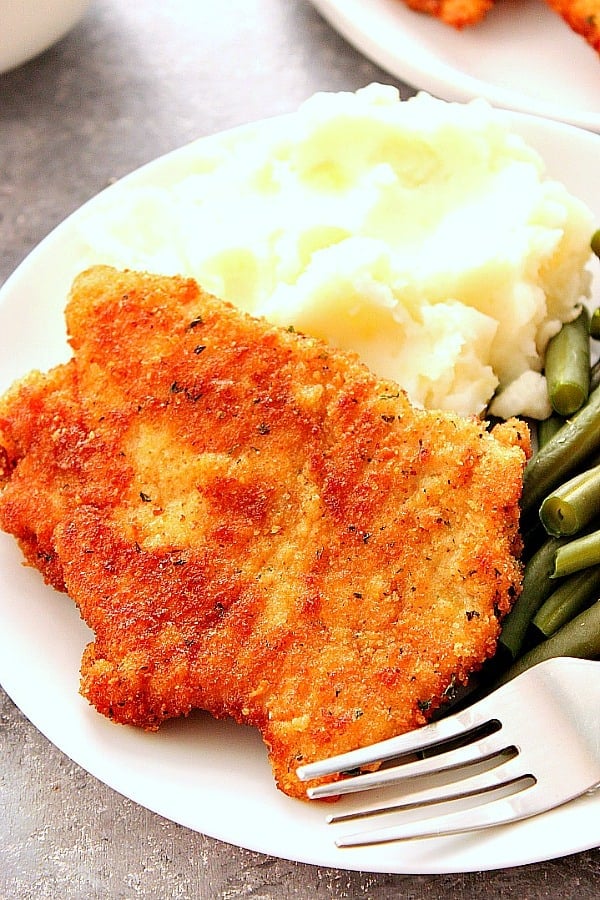 Pork schnitzel with mashed potatoes and green beans on white plate.