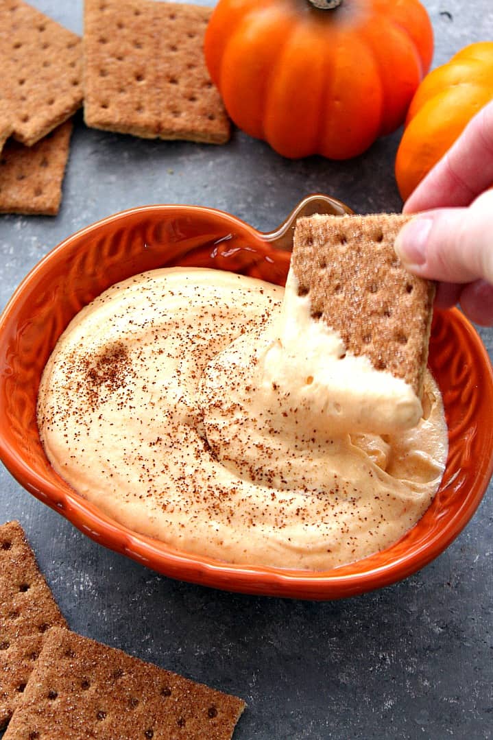 Side shot of pumpkin cheesecake dip in pumpkin dish with cracker dipped in dip.