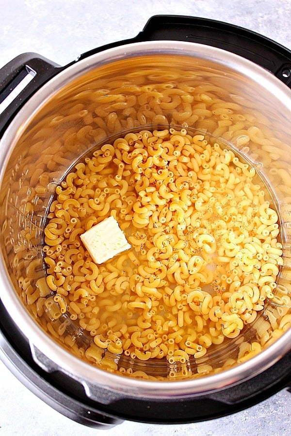 Overhead shot of macaroni pasta in water, with pieces of butter on top, in Instant Pot.