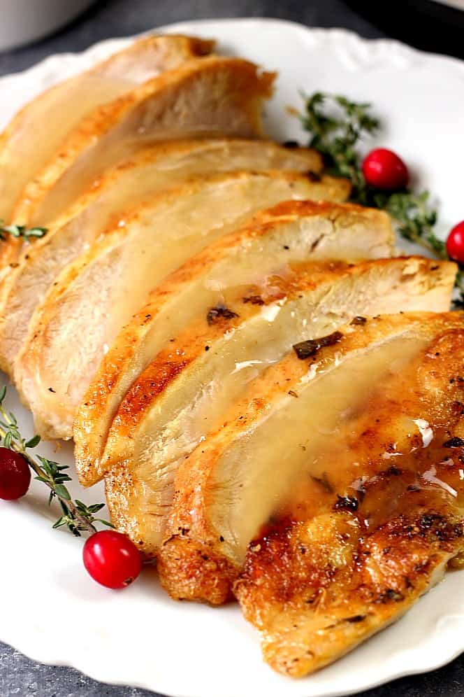 Side shot of sliced turkey breast with gravy on white platter.