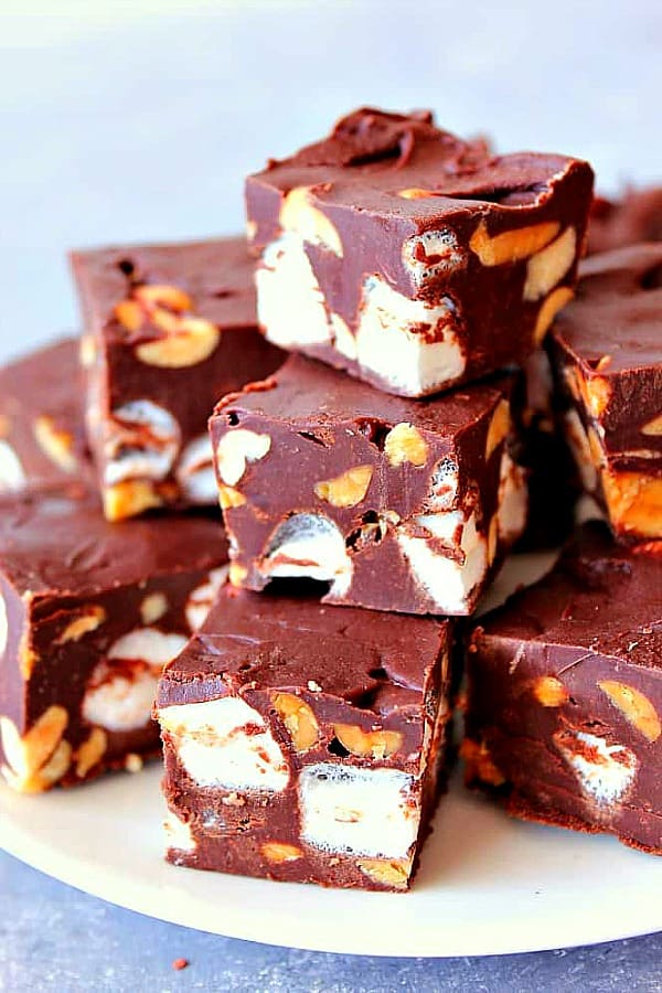 Squares of chocolate fudge with peanuts and marshmallows on a white plate.