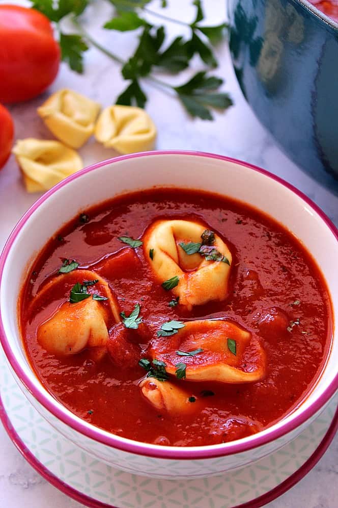 Overhead shot of tomato tortellini soup in white bowl with purple rim.