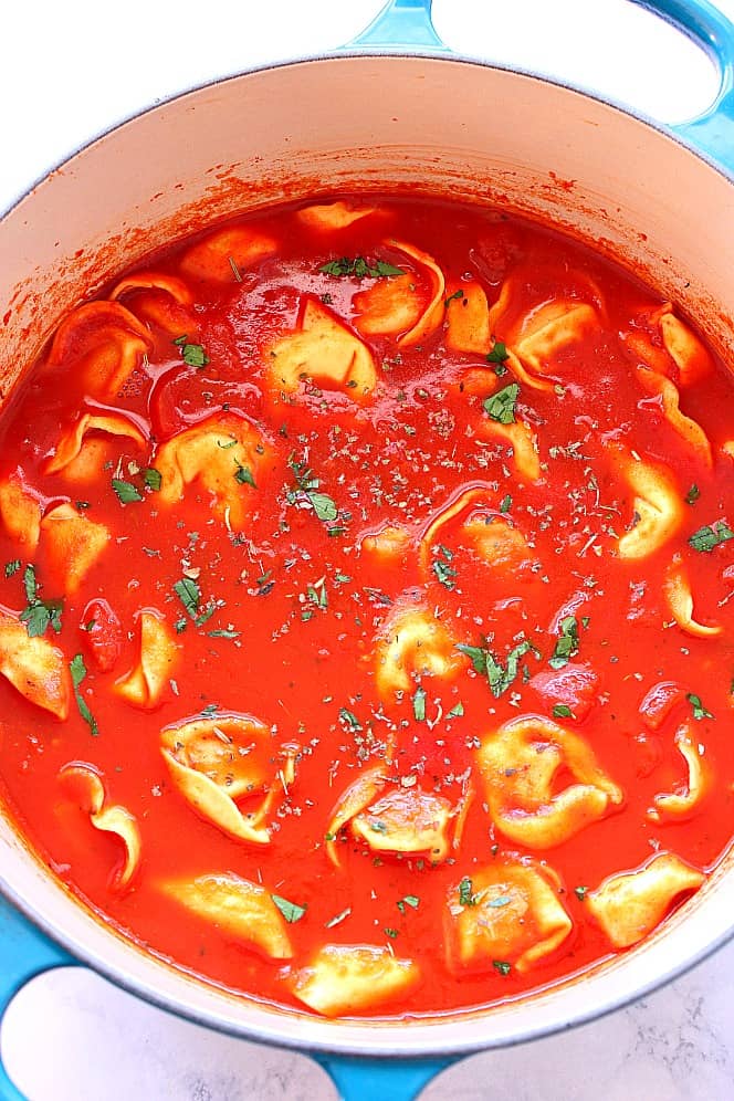 Overhead shot of tomato soup with tortellini pasta in cast iron Dutch oven.