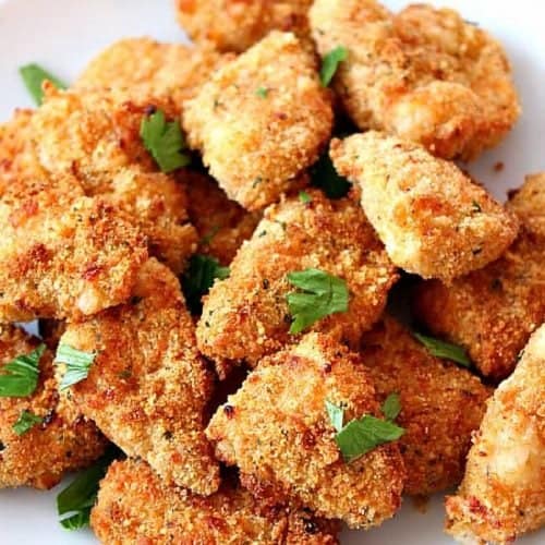 Square image of chicken nuggets with parsley on a white plate.