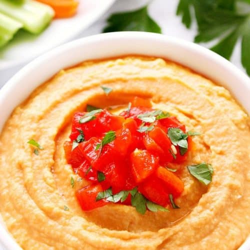 Roasted Red Pepper Hummus in a white bowl on marble board.