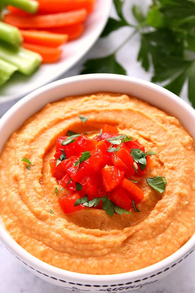 Roasted Red Pepper Hummus in a white bowl on marble board.