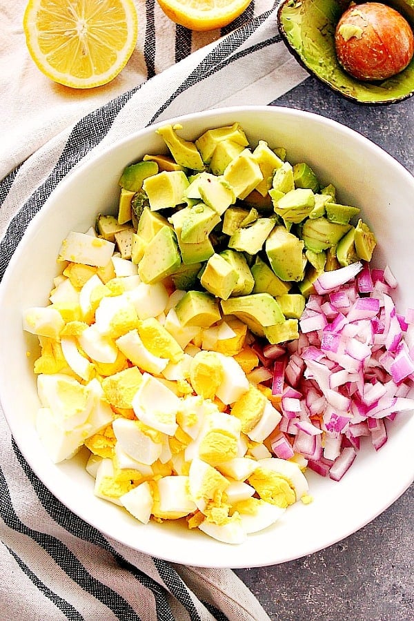 Overhead shot of chopped avocados, red onion and eggs in salad bowl.