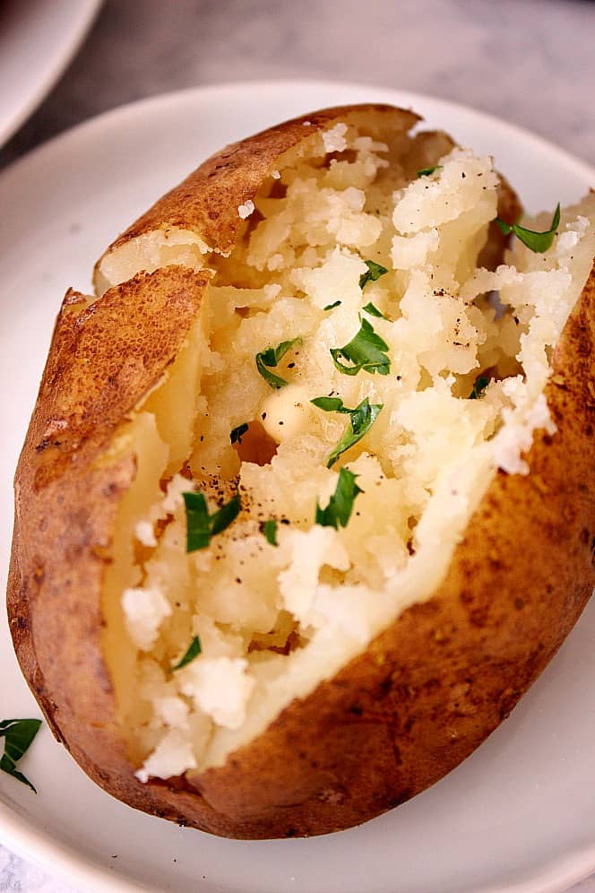 Close up shot of baked potato sliced in half on white plate.