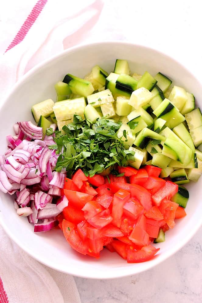 chopped cucumbers, tomatoes, red onion and parsley in a bowl